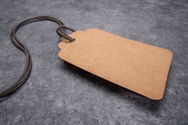 blank paper price tag with a twine against gray textured handmade paper, shopping concept - Фото, изображение