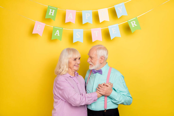 Portrait of two attractive cheerful tender grey-haired spouses spending easter day isolated over bright yellow color background - Zdjęcie, obraz