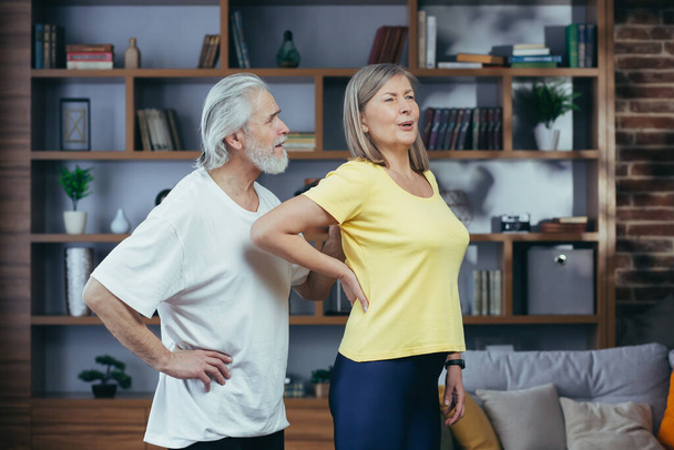 Senior husband massaging his wife's back, gray-haired retired couple at home during fitness class - Photo, Image