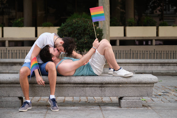 Homopari nauraa ja halailee penkillä pitäen LGBT-lippuja. - Valokuva, kuva