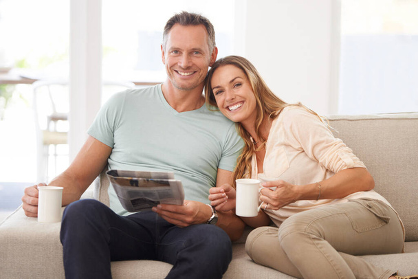 朝の新聞を共有する。幸せな夫婦の肖像画彼らのソファの上で新聞を読んで. - 写真・画像