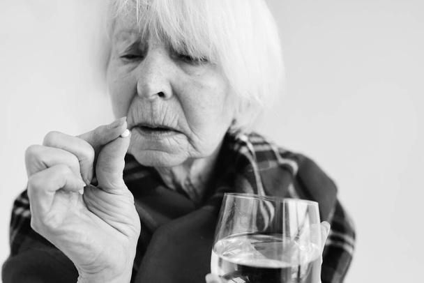 monochromatický portrét starší ženy v kostkovaných kostkách s pilulkou a sklenicí vody. Zdravotní péče, zralý věk, koncepce onemocnění - Fotografie, Obrázek