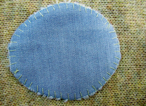 Patch in tessuto per maglia Il gomito è stato patchato con un rottame ovale di tessuto denim blu e cucito con un punto frusta. - Foto, immagini