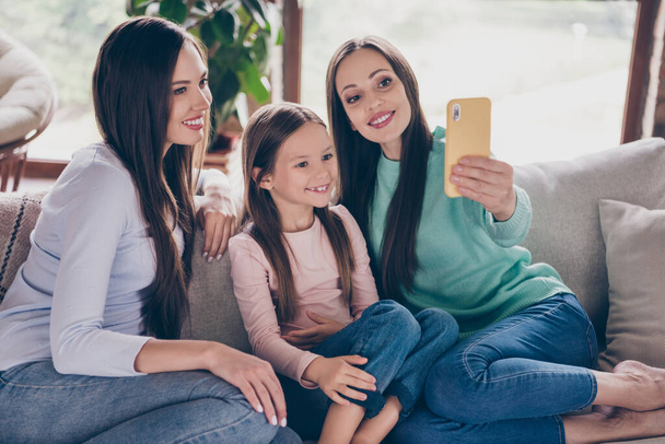 Photo of three charming girl shoot selfie picture speak video call cellphone sitting divan flat indoors - Foto, Imagen