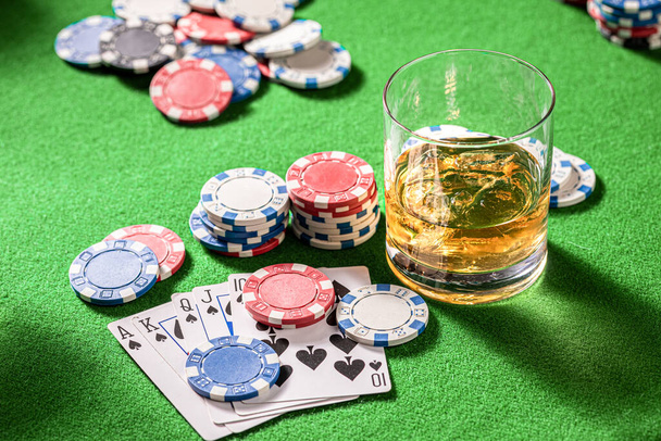 Green gambling table with whisky, cards and chips. Glass of bourbon with ice on gambling table with cards and chips. - 写真・画像