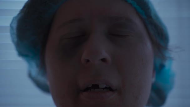 Una mujer caucásica con traumatismos faciales y dentales y lesiones mira tristemente a la cámara en su bata de hospital en el hospital - Imágenes, Vídeo