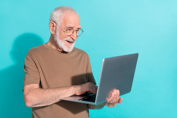 Portrait of attractive cheerful focused grey-haired man using laptop writing letter isolated over bright blue color background - Φωτογραφία, εικόνα