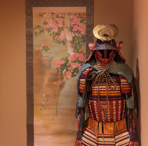 Бронекостюм самурая, стоящий рядом с японской картиной - Фото, изображение