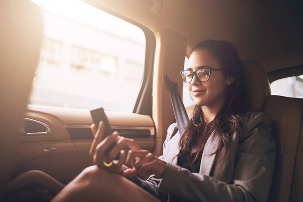 Confirming her important meetings for the day. Shot of a young businesswoman texting on a cellphone in the backseat of a car. - Foto, afbeelding