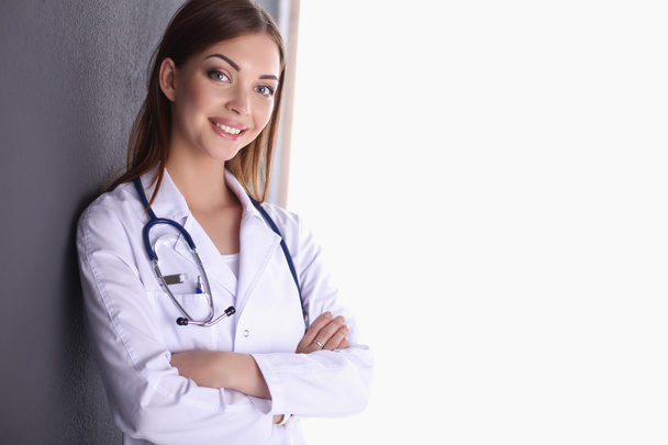 Doctor woman with stethoscope standing near grey wall - Fotó, kép