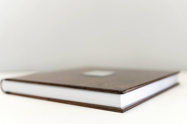 Fotobuch aus Holz auf hellem Hintergrund. Metallschild. Ein braunes Buch mit Holzeinband liegt auf einem Leinentuch. Idee, Konzept, Innovation oder Planung - Foto, Bild