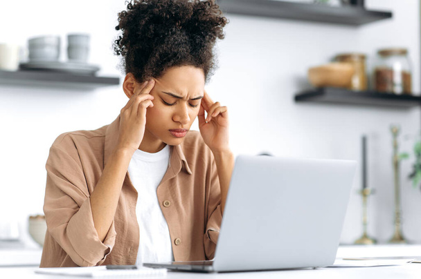 Unavená Afroameričanka z práce v laptopu, sedící doma u stolu v kuchyni, zavírá oči, masíruje si spánky, má migrénu, bolest hlavy, napětí, potřebuje si odpočinout, přestávku - Fotografie, Obrázek