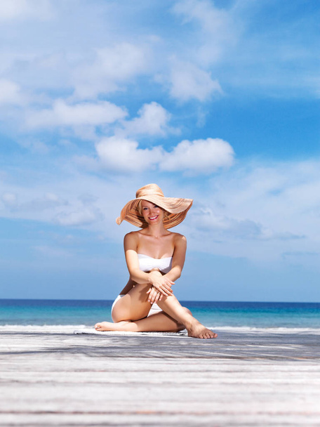 Piękne wakacje na plaży. Portret seksownej młodej kobiety w białym bikini i kapeluszu pozującej nad morzem. - Zdjęcie, obraz