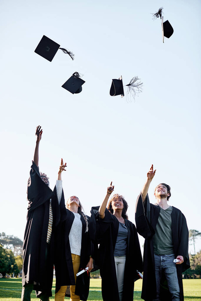 Todas las recompensas valen la pena. Foto de un grupo de estudiantes lanzando sus sombreros al aire en el día de la graduación. - Foto, imagen