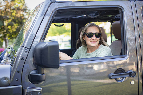 Hymyilevä ja onnistunut onnellinen aikuinen nainen ajaa autoa. Istuminen kuljettajan istuimella sen jälkeen, kun olet poistunut jälleenmyyntisopimuksesta uuden auton oston jälkeen - Valokuva, kuva