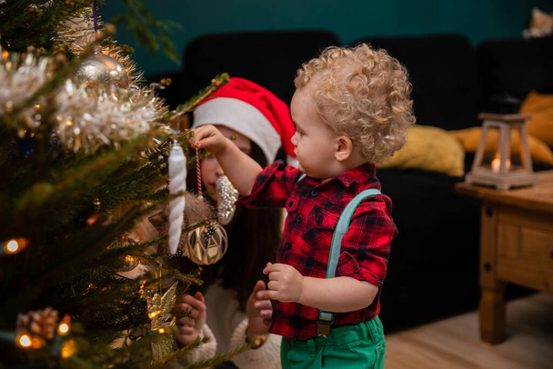 The little boy hangs the ornaments on the Christmas tree and the older sister watches. - Fotó, kép
