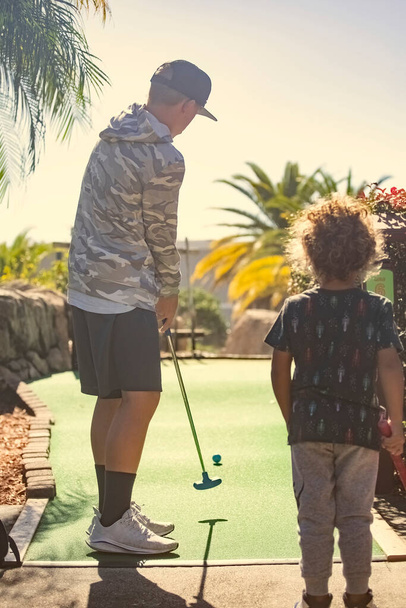 Rear view photo of two boys playing mini golf while on a fun family vacation together. - Photo, Image