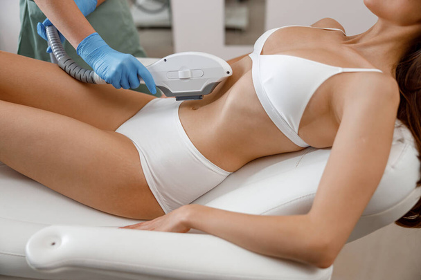 Slim young woman getting photo epilation with ipl machine in beauty salon - Foto, immagini