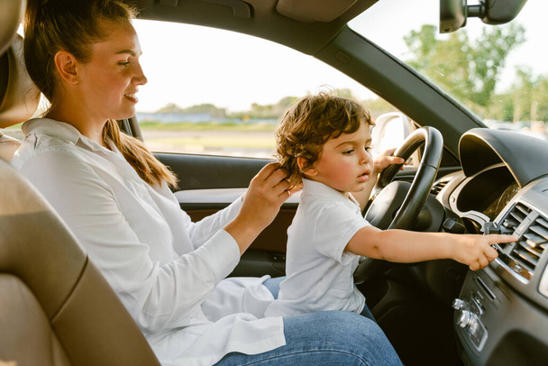 Молода біла жінка посміхається і грає зі своїм сином, сидячи в машині
 - Фото, зображення