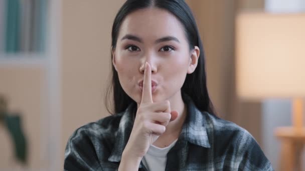 Portrait asian ethnic korean woman point with finger near mouth Chinese Japanese girl makes hush quiet gesture showing secret sign asks silent confidential secrecy information looking at camera indoor - Footage, Video