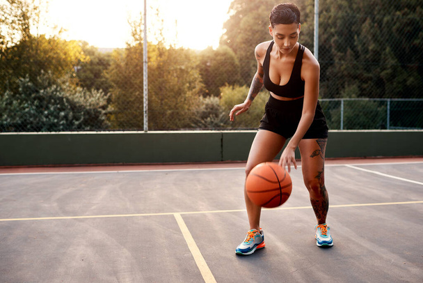 Zahřívání je nezbytné. Dlouhý záběr atraktivní mladé sportovkyně stojící sama na basketbalovém hřišti a zahřívá se s míčem. - Fotografie, Obrázek