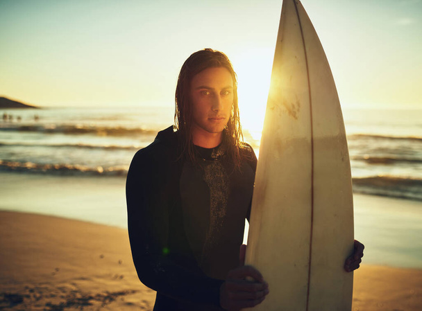 Being a surfer is simply in my blood. Portrait of a young man standing with a surfboard at the beach. - Foto, Imagem