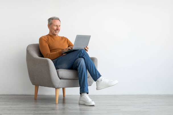 Homme mature souriant confiant utilisant un ordinateur portable à la maison - Photo, image