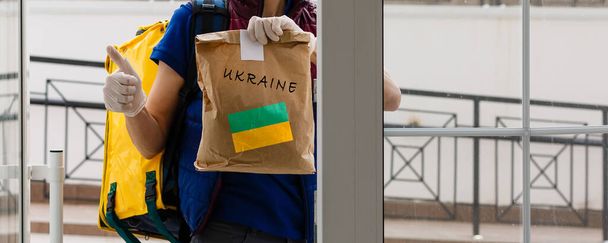 Ένας άνδρας κρατά ένα κουτί βοήθειας για τους Ουκρανούς πρόσφυγες και τους φτωχούς πολίτες που βρίσκονται σε έναν πόλεμο μεταξύ Ουκρανίας και Ρωσίας. Σχέδιο ανθρωπιστικής βοήθειας. Δωρεά για πρόσφυγες. - Φωτογραφία, εικόνα