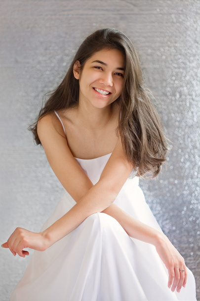 Beautiful biracial teen girl in white dress, sitting arms crosse - 写真・画像