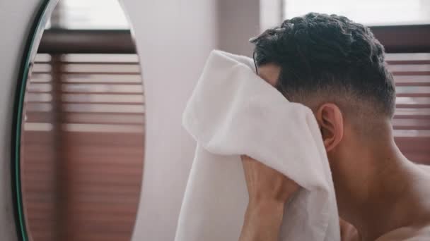 Primer plano vista lateral árabe barbudo barbudo hombre hombre hombre lavando la cara con agua tibia en el baño en casa en el hotel mirando en espejo reflejo sonriente limpiar la cara húmeda con toalla de baño blanca higiene de la mañana - Metraje, vídeo