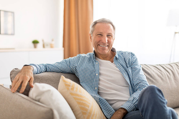 Χαμογελώντας ώριμος άντρας κάθεται στον καναπέ και ποζάρει - Φωτογραφία, εικόνα