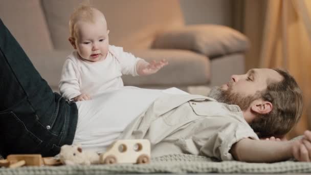 Kavkazský rodinný otec s malým synem leží na podlaze při domácí hře. Děvčátko chlapec novorozeně dítě plazit se přes tatínek péče o dítě otcovství školky uvnitř. Dětská rodičovská láska - Záběry, video