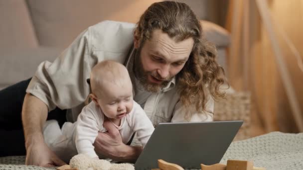 Valkoihoinen parrakas isä, jolla on vastasyntynyt lapsi, käyttää kannettavaa internetiä online-videopuhelukonferenssissa kotona. Isä vanhempi pieni tytär poika lapsi vauva katso tietokoneen näytön lapsi leikkiä lelu - Materiaali, video