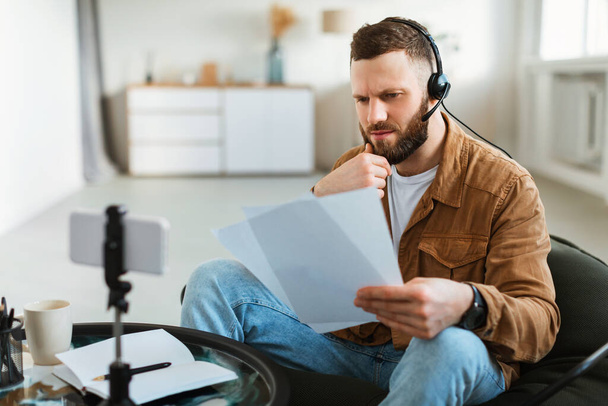 Pensativo masculino leitura papéis fazendo vídeo em Smartphone em casa - Foto, Imagem