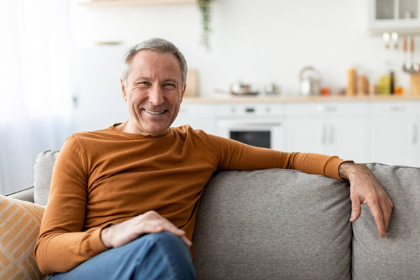 Smiling mature man sitting on the couch and posing - Photo, Image