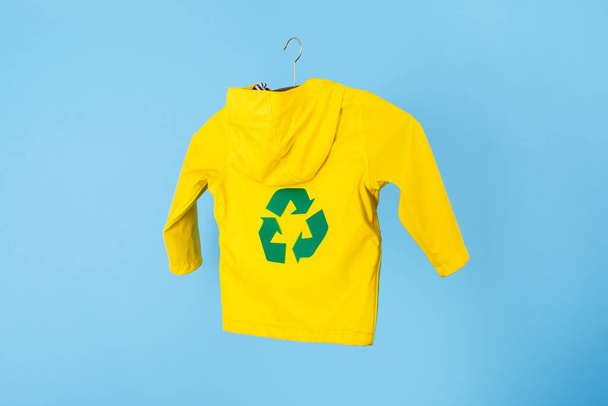 Recycling von Regenbekleidung. gebrauchte Oberbekleidung. Ökologischer und nachhaltiger Lebensstil. Recycling-grünes Schild auf gelbem Regen auf blauem Hintergrund. Hochwertiges Foto - Foto, Bild