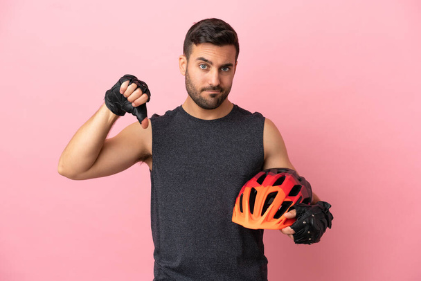 Young cyclist man isolated on pink background showing thumb down with negative expression - Photo, Image