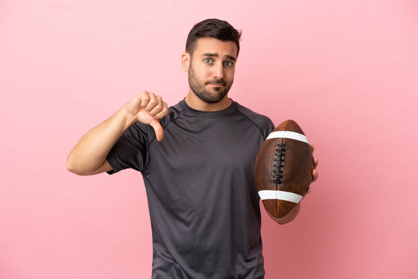Young caucasian man playing rugby isolated on pink background showing thumb down with negative expression - Photo, Image