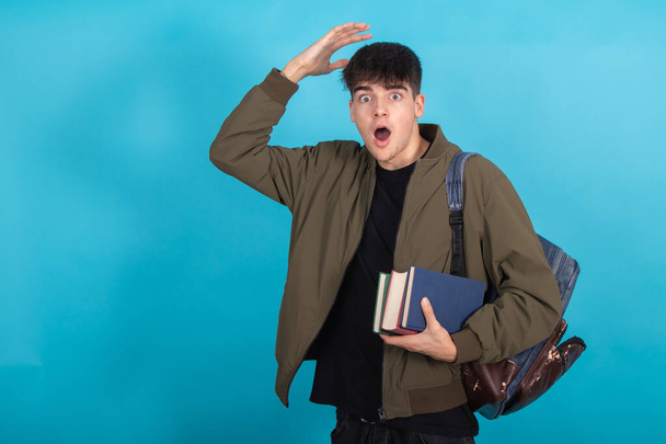 étudiant avec des livres et sac à dos étonné isolé sur fond bleu - Photo, image