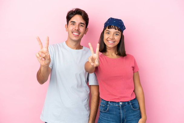 Νεαρό ζευγάρι απομονωμένο σε ροζ φόντο χαμογελώντας και δείχνοντας το σύμβολο της νίκης - Φωτογραφία, εικόνα