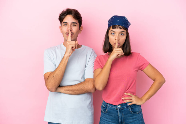 Νεαρό ζευγάρι απομονωμένο σε ροζ φόντο που δείχνει ένα σημάδι κλεισίματος του στόματος και χειρονομία σιωπής - Φωτογραφία, εικόνα