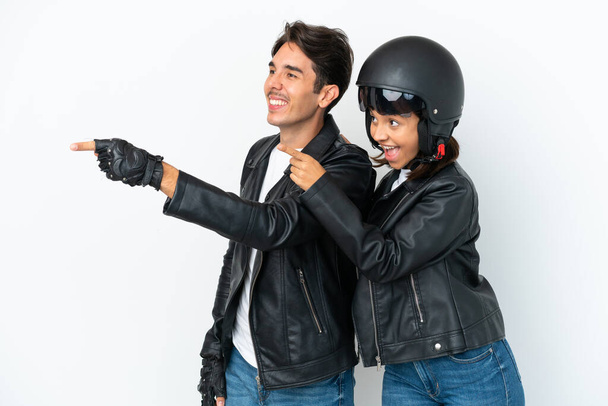 Молода змішана пара гонок з мотоциклетним шоломом ізольована на білому тлі, вказуючи на бік, щоб представити продукт
 - Фото, зображення