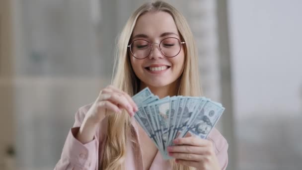 Boldog kaukázusi üzletasszony szemüvegben gazdag sikeres lány győztes nő dob pénzt a levegőben ujjongás bankjegyekkel kap pénzügyi haszon győzelem scatter dollár győzelem beltéri közeli portré - Felvétel, videó