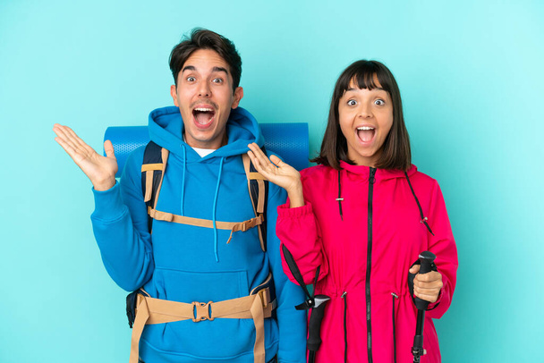 若い登山家のカップルは驚きとショックを受けた表情で青の背景に隔離されました - 写真・画像