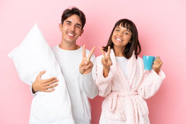 Young couple in pajamas isolated on pink background smiling and showing victory sign - Foto, immagini