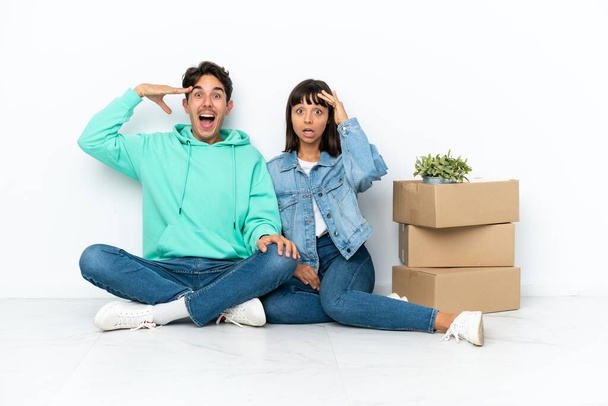 Молодая пара делает шаг, поднимая коробку с вещами, сидя на полу изолированы на белом фоне только что понял что-то и намеревается решение - Фото, изображение