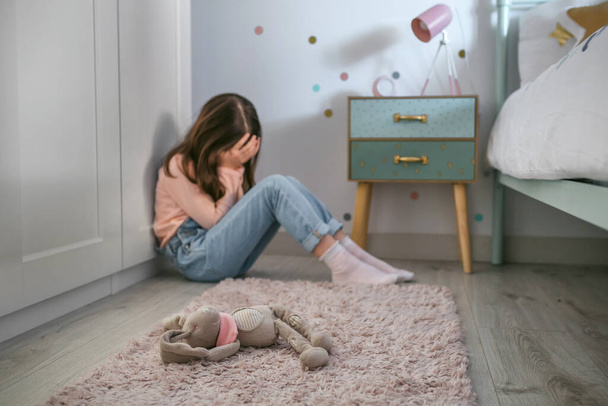 Sad girl sitting on the floor of her bedroom with stuffed toy lying - Zdjęcie, obraz