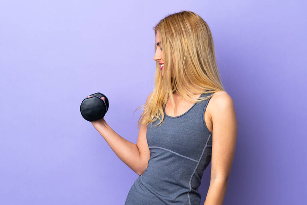 Joven mujer deportiva rubia haciendo levantamiento de pesas sobre fondo púrpura aislado con expresión feliz - Foto, imagen