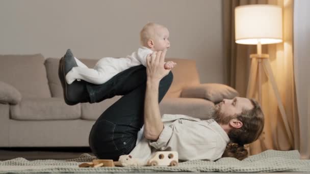 Happy male father parent caucasian dad lifting cute little kid daughter son up fly pretend airplane having fun enjoying lying on floor at home adorable small child newborn infant playing with daddy - Footage, Video