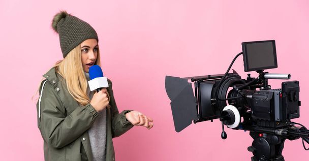 Δημοσιογράφος γυναίκα κρατώντας ένα μικρόφωνο και αναφέροντας ειδήσεις σε απομονωμένο ροζ φόντο - Φωτογραφία, εικόνα